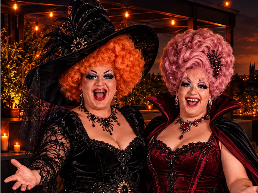 Two drag queens dressed as a witch and a vampire on The Rooftop terrace at night, with Canterbury lit up behind