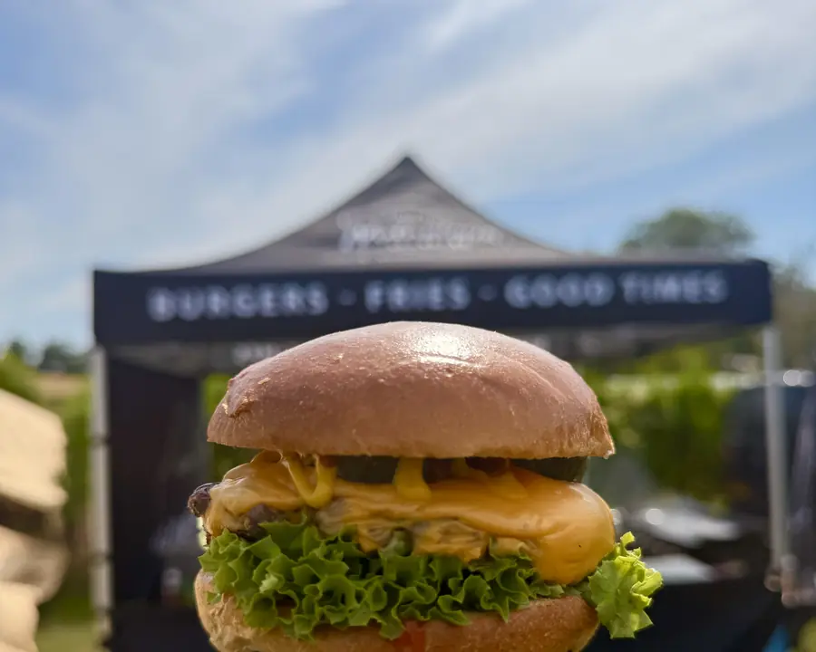 Burger held up in front of the Notorious 'Burgers, Fries, Good Times' gazebo