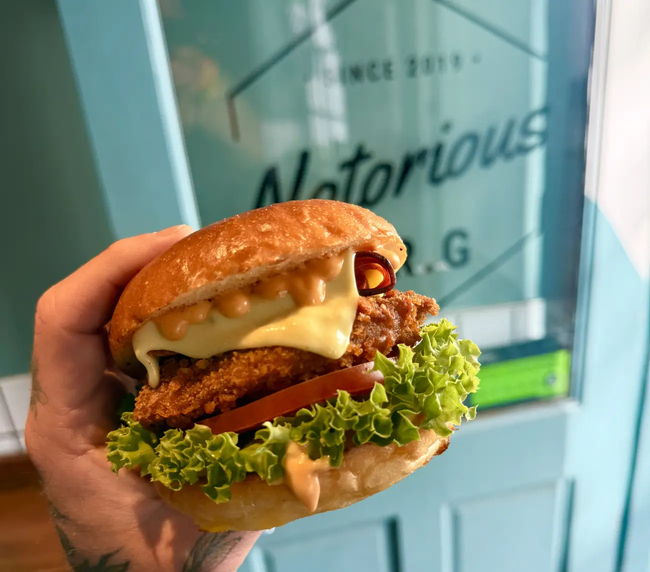 Fried chicken burger held up outside the teal Notorious B.R.G shopfront on Castle Street, Canterbury