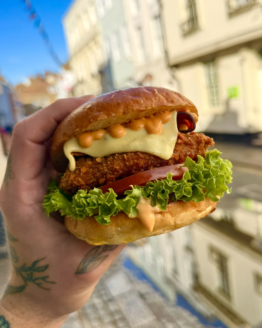 Vegan El Pollo burger with crispy vegan 'chicken', cheese, tomato and lettuce, held up on Castle Street, Canterbury